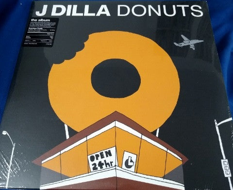 A vinyl LP record album cover for J Dilla's album 'Donuts'. The cover features a graphic of a donut on a black background with yellow and white accents, and text indicating the album title and artist name.