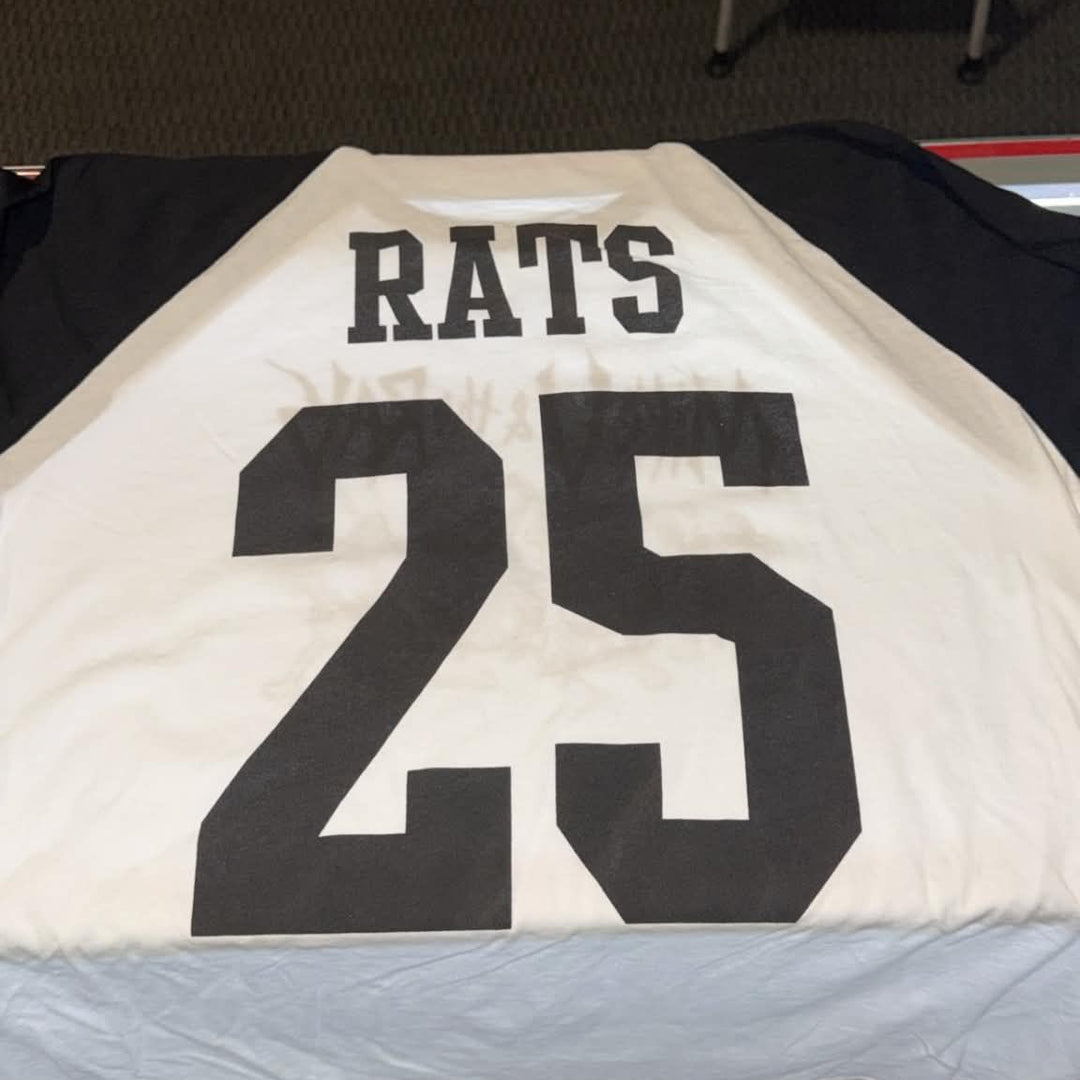 A white and black baseball-style jersey laid flat on a table, showing the back with the word 'RATS' and the number '25' in large black block letters.