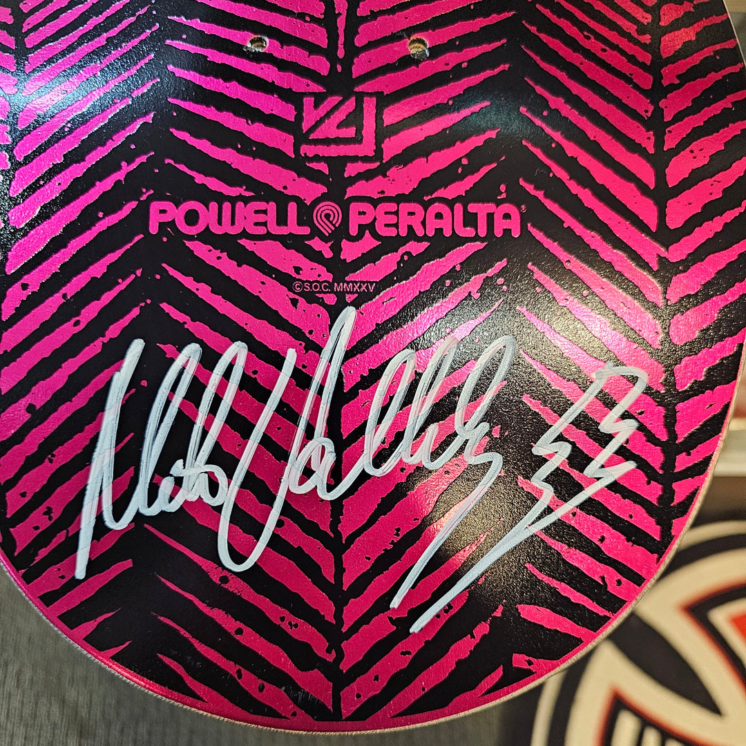 Close-up of a Powell Peralta Mike Vallely signed skateboard deck with a pink and black pattern and signature.