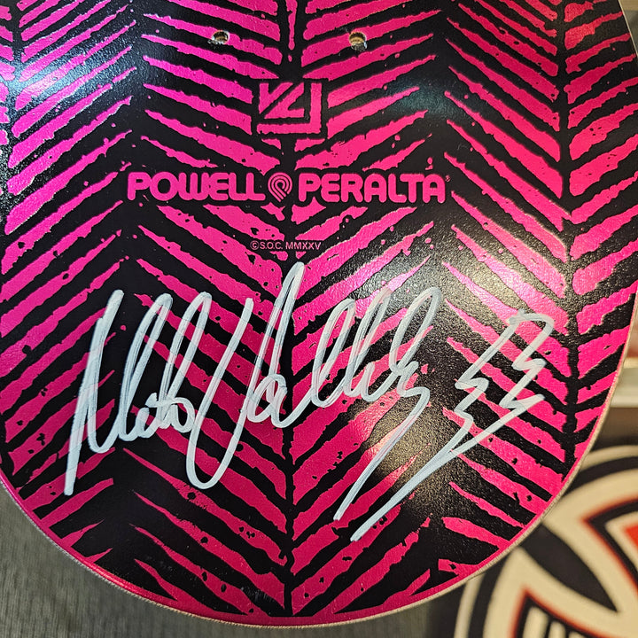 Close-up of a Powell Peralta Mike Vallely signed skateboard deck with a pink and black pattern and signature.