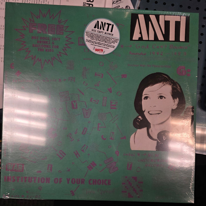 Vinyl record with a green cover featuring a face and text, on a cluttered surface.